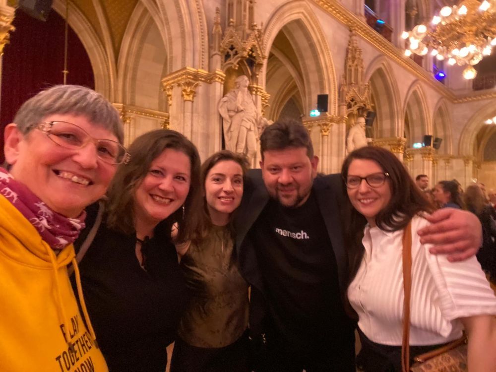 Vier Frauen und ein Mann posieren lächelnd für ein Gruppenfoto in einem prächtig beleuchteten Saal mit gotischer Architektur, hohen Gewölben und Statuen. Die Stimmung wirkt fröhlich und festlich.