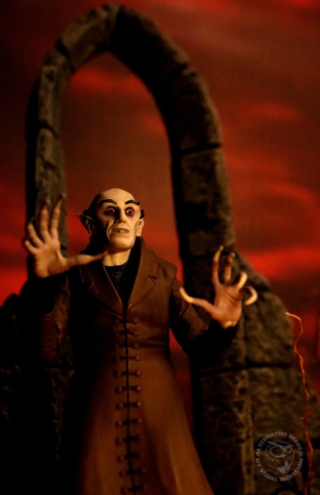 Count Orlok caught in the dawn's early light. He stands in front of a castle ruin with a blood red sky behind him. 