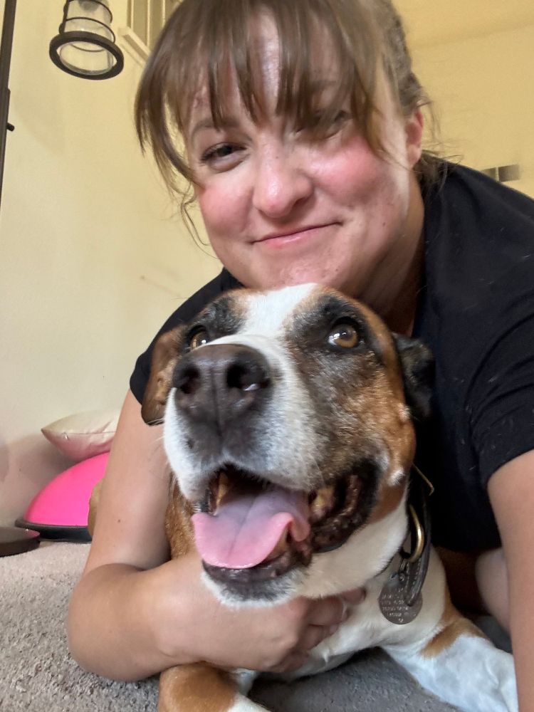 A happy picture of me mostly laying on top of Lucy, a brown and white staffie pitbull mix. I look happy with my chin rest on top of her head. She looks confused trying to see what’s on top of her. She looks sweet and undisturbed 