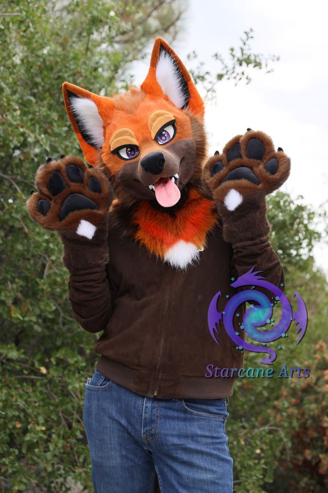 A fox partial fursuiter is seen standing in a forest environment. 