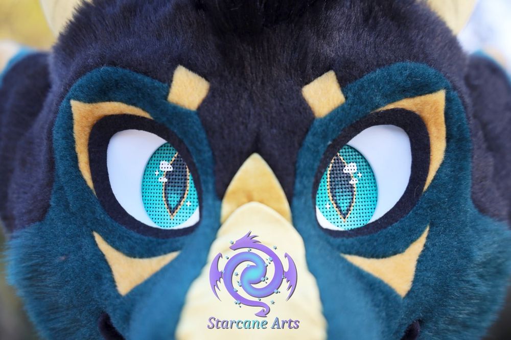 A close-up of a teal and black fursuit face gold markings, with the seafoam eyes being the primary focus. Golden scalescan be seen running along the top of the muzzle.

The Starcane Arts logo is visible as a watermark just above the scales.