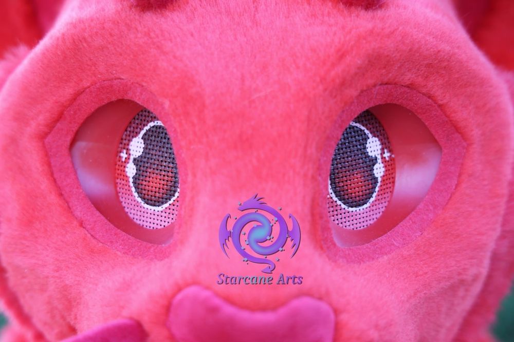 A close-up of an all red fursuit face with the red eyes being the primary focus. A red nose can be seen just at the bottom of the frame.

The Starcane Arts logo is visible as a watermark just above the nose. 