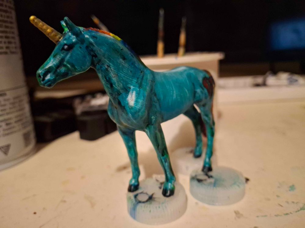 Greenish blue unicorn with rainbow mane and gold horn. Broken heart image on one hip, and storm cloud on the other