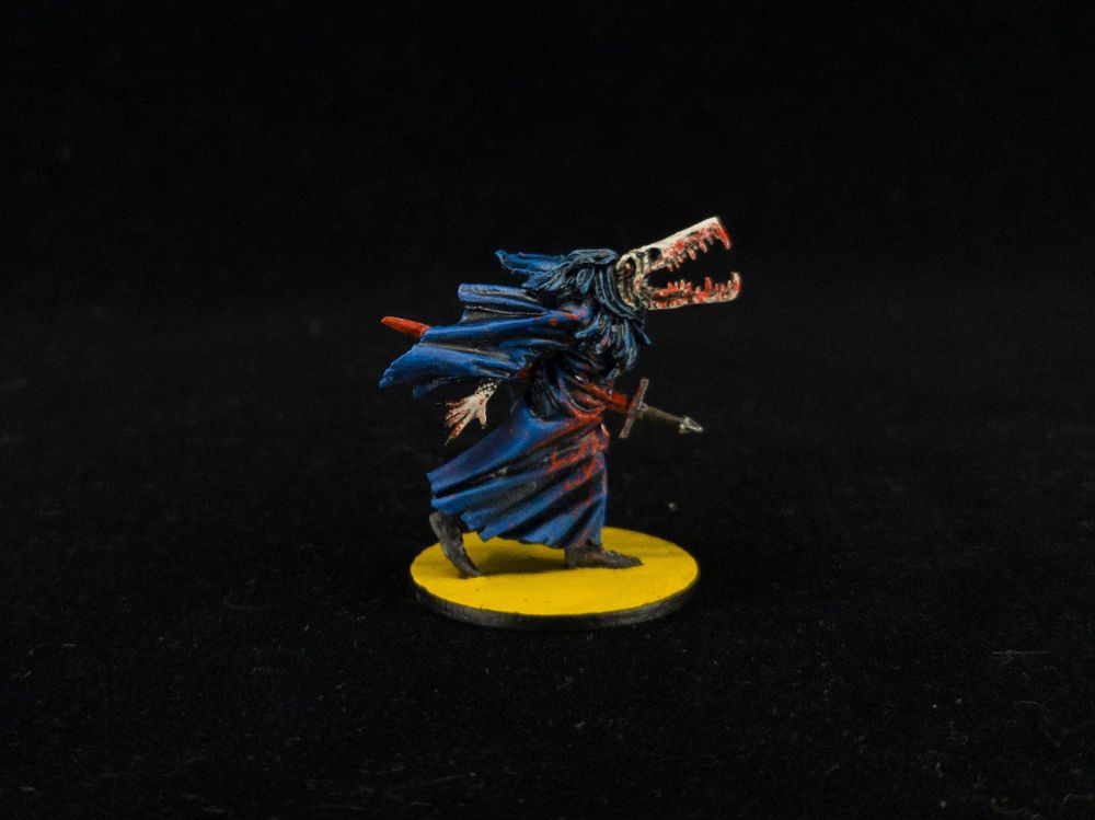 Painted mini of a sort of gator-man skeleton in a blue robe, impaled on a sword, with blood splattered everywhere including its bright yellow base.
