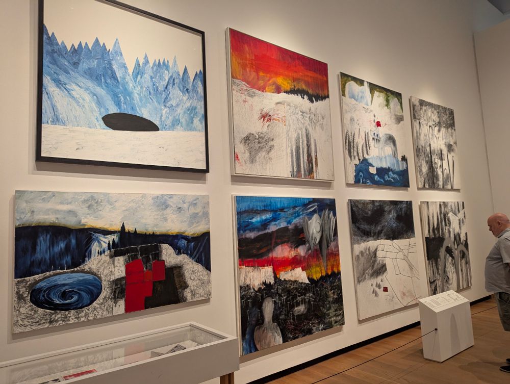 A wall of 8 large paintings by Stanley Donwood in an art exhibition. From left to right, top to bottom: "Hole", "Residential Nemesis", "Avert Your Eyes", "Minos Wall III", "War Village", "Get out before Saturday", "Hotels and a swimming pool", "Minos Wall II"