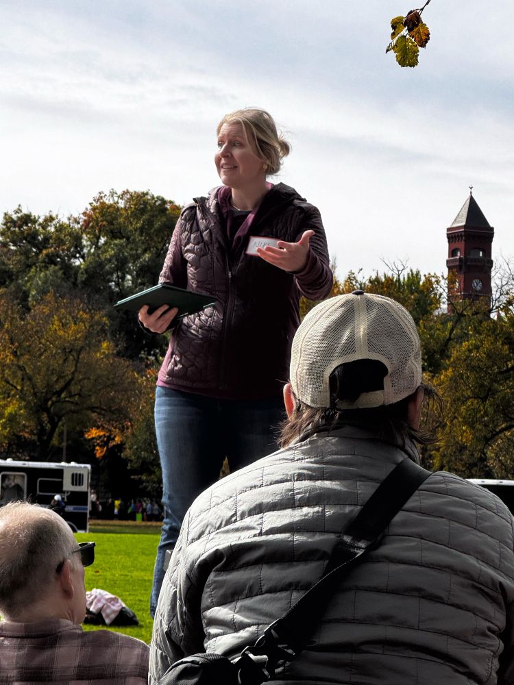 Niki Hemmer standing on a park bench talking to a crowd.