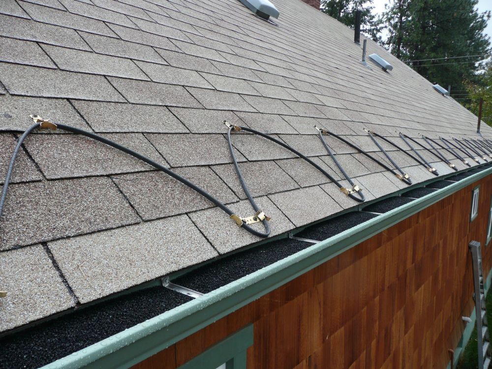 A picture of the lower edge of a roof on a house. Some sort of electrical wire zigzags up and down across the length of the roof. It is held down by brackets. This wire heats up after it is plugged in and turned on in order to clear snow and ice from the edge of the roof to prevent ice dams from causing damage.