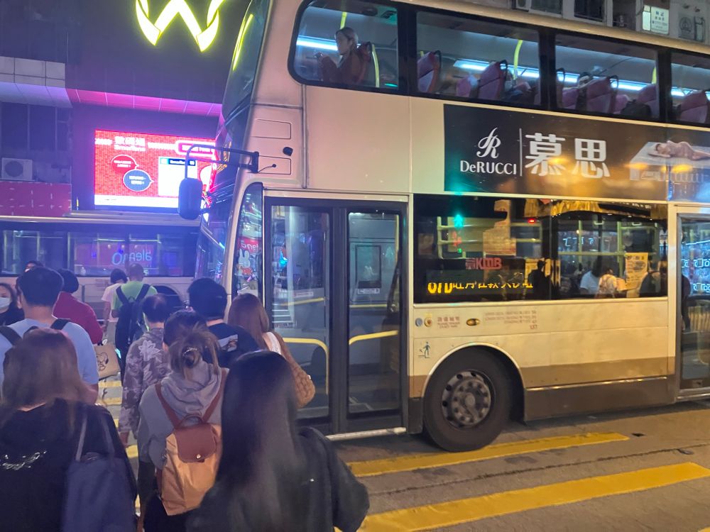 A public bus has stopped half way through a zebra crossing, the pedestrians are crossing. 