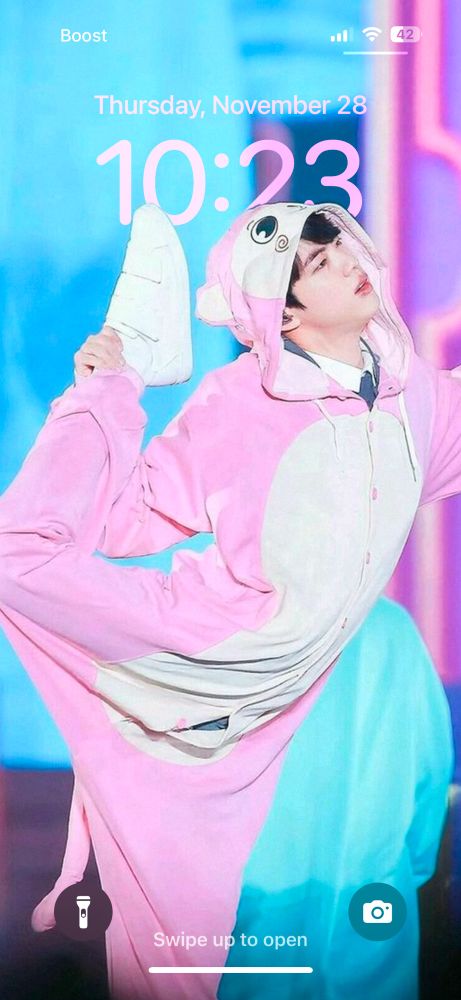 Jin in pink animal onesie touching his foot to his head like an ice skater in a spin.