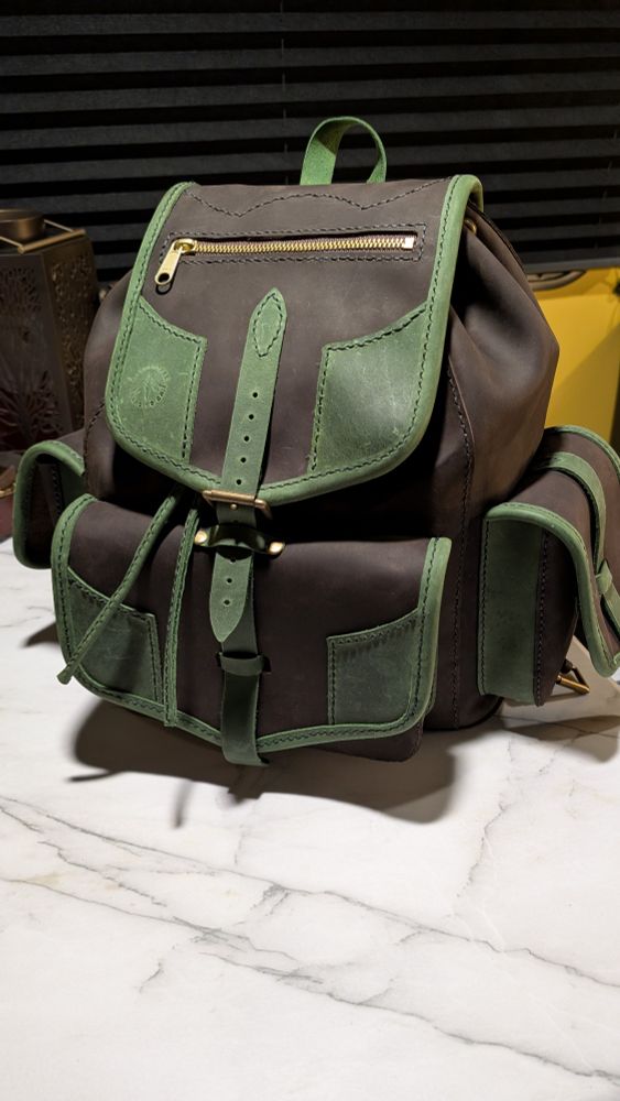 A hand sewn brown and green leather backpack on a white marble table.