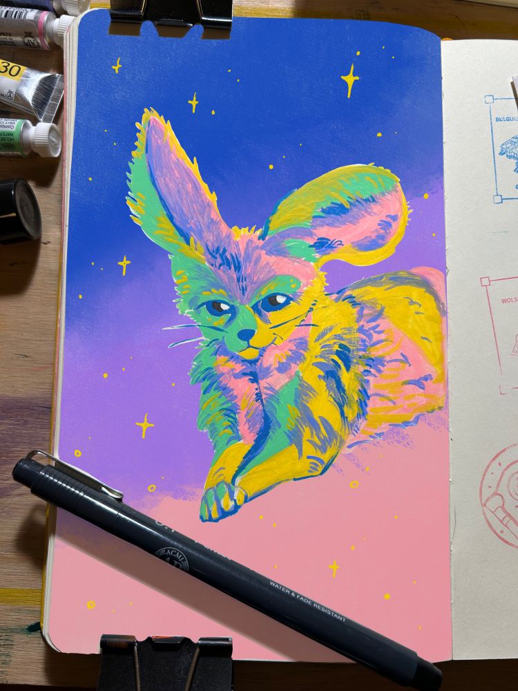 A colorful fennec fox watercolor painting in pastel colors. It’s in an open sketchbook, the paint tubes and a pen used for the painting are next to the painting. The digital background of the animal has a moody pink galaxy vibe with stars around the fox. 