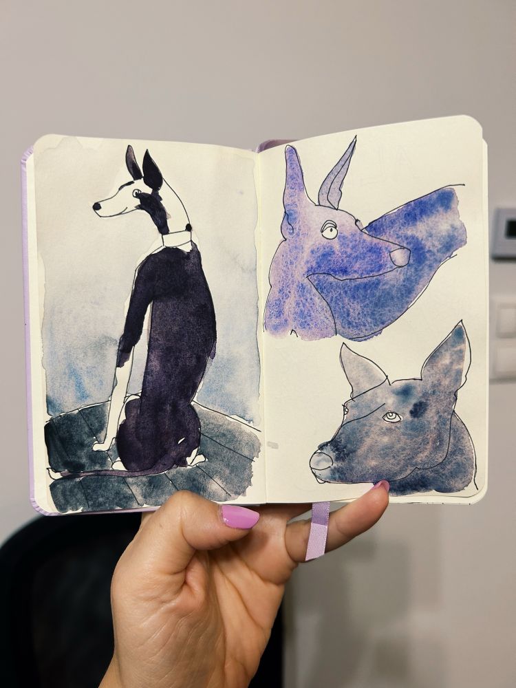 Three watercolor paintings of dogs in a sketchbook