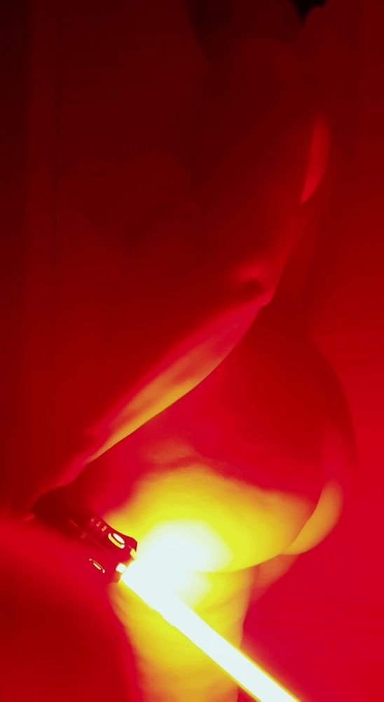 Naked, curvy person with a red lightsaber held in front of them, highlighting the curves of their ass.