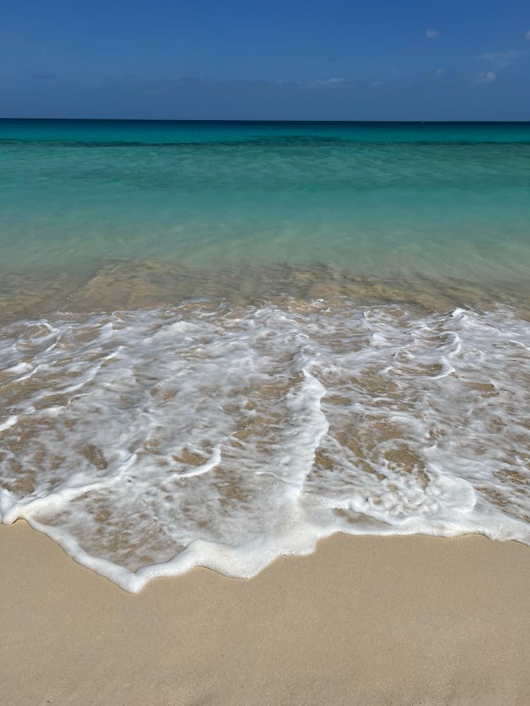 der Atlantik in verschiedenen Blau- und Purpurtönen, weiße Schaumkronen über hellen Strand im Vordergrund