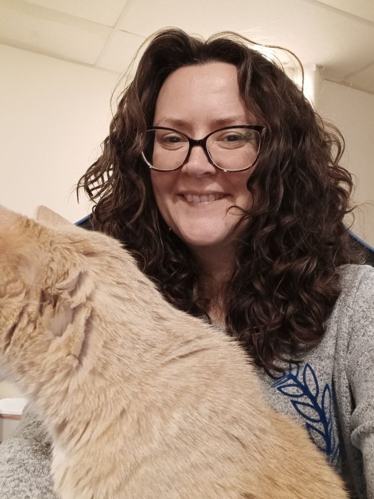 Me smiling in the background (brown hair down and wearing a grey light sweater) with my champagne blind tabby, Blondie.