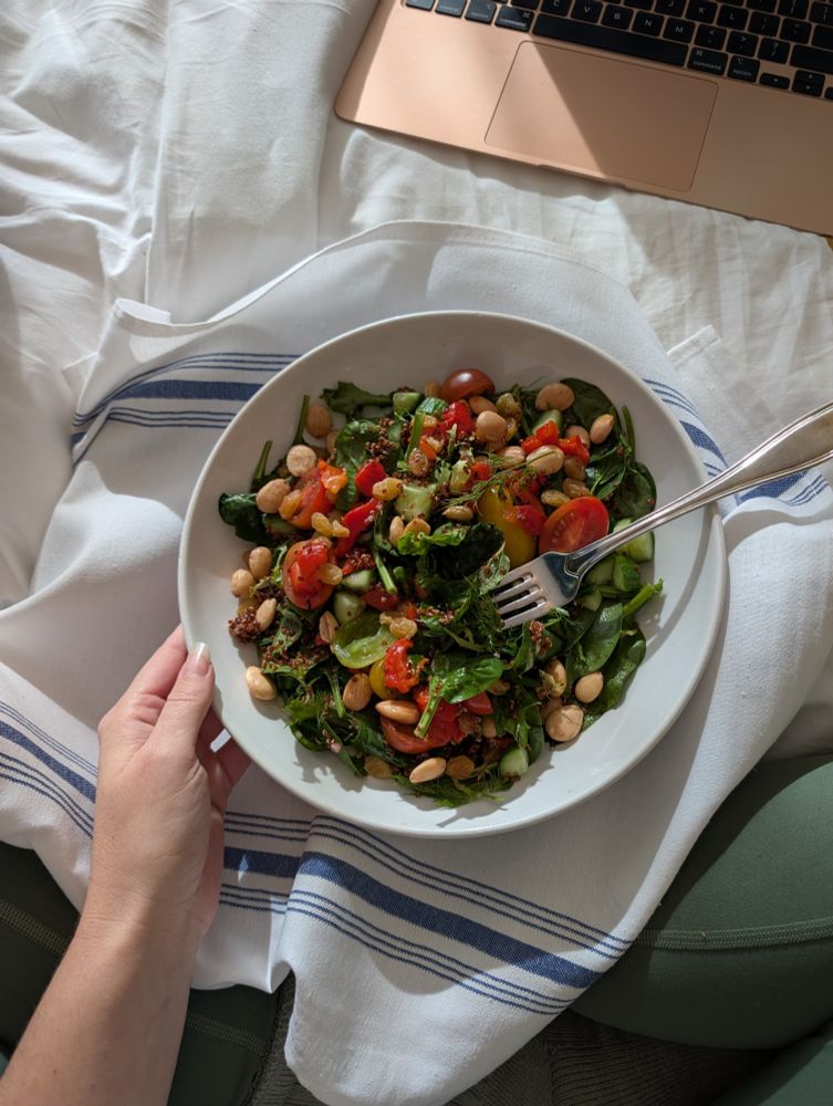A green and quinoa salad in a bowl on a white and blue cloth napkin. A white hand holds the bowl lightly.