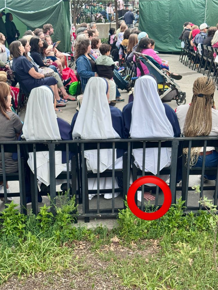 A red circle drawn over a photo of three seated nuns. In the middle of a circle is a hand underneath one nun’s chair. 
