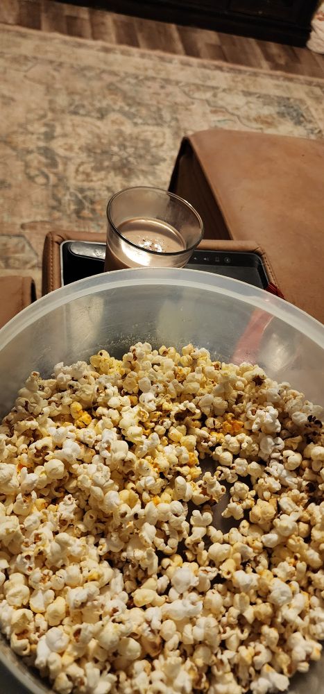 A big bowl of cheese powder dusted popcorn and a glass of chocolate milk behind it.