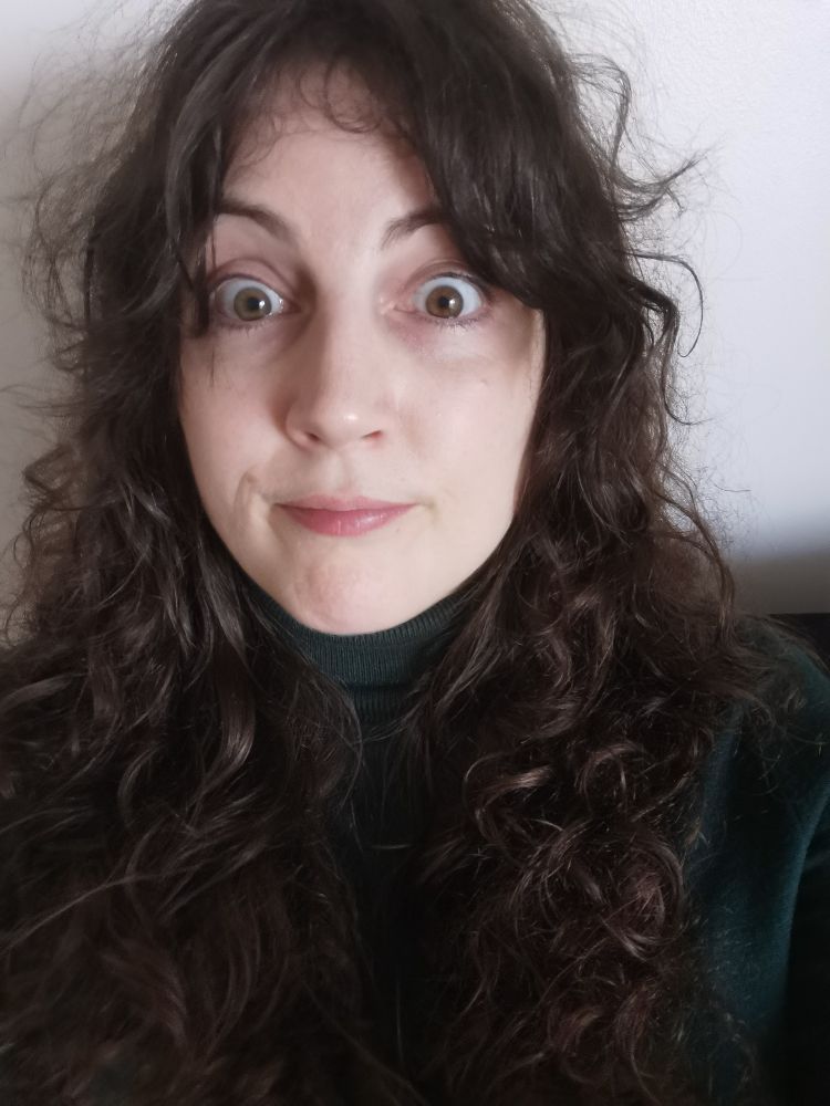 It's a selfie of me, Jennifer Leask. A whyte nonbinary women with long brown hair, wearing a forest green turtleneck. My expression is giving deer in the headlights, slow down. My hair is a bit frizzy at the top and kind of curly and wavy. 