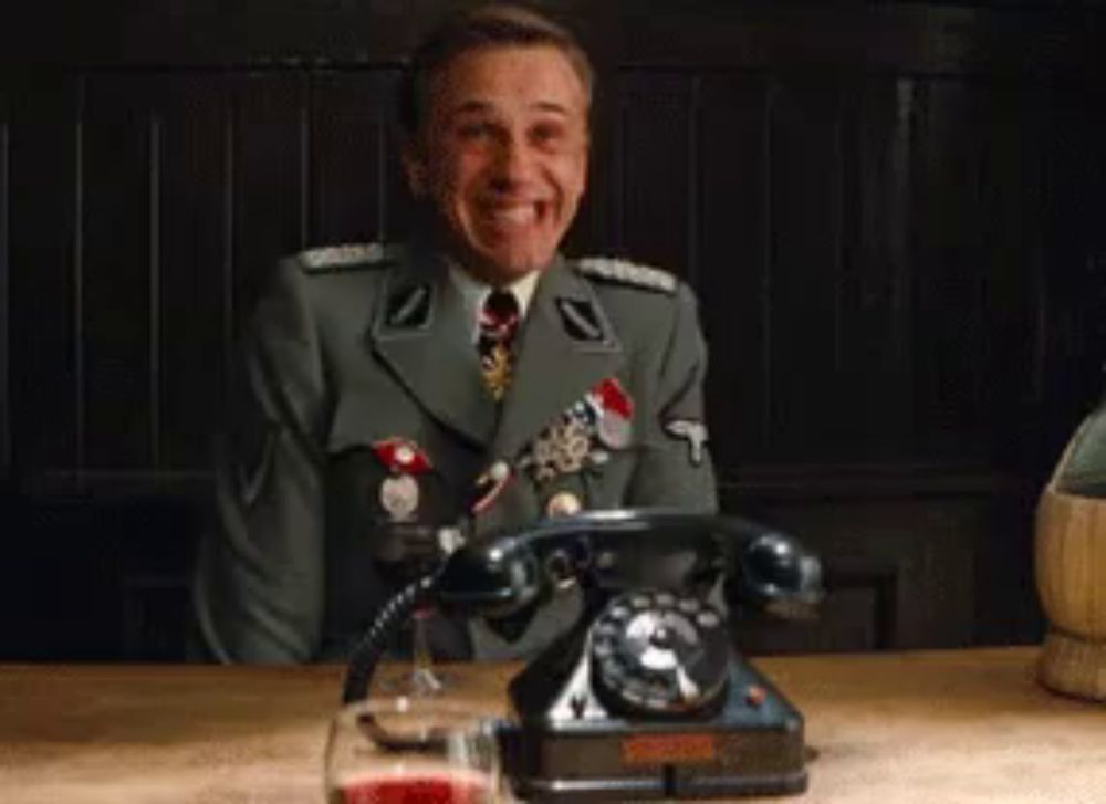 a man in a military uniform is sitting at a table with a telephone and a glass of wine