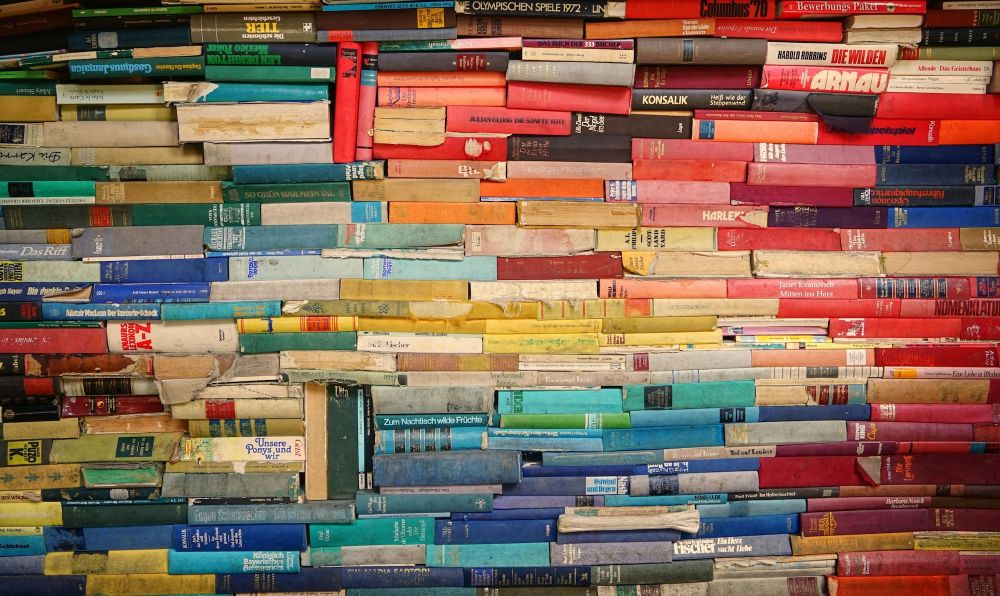A pile of books with coloured spines showing the pattern of a rainbow