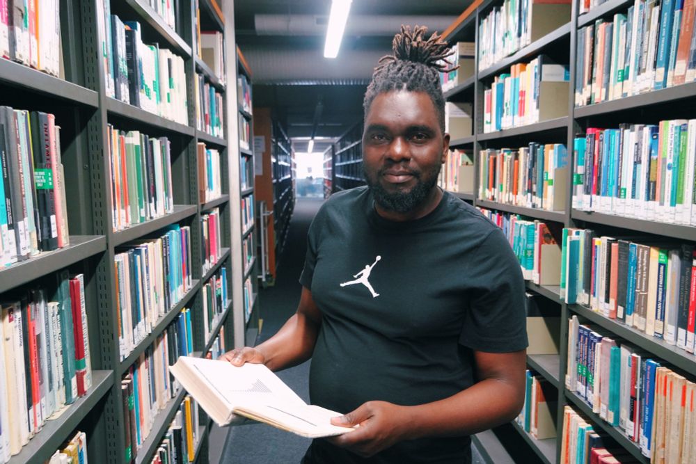 A man stands in the aisle of the SOAS Library holding an open book