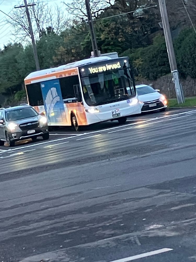 A bus in traffic with the words “you are loved” on its electronic display. The letter o is heart shaped.