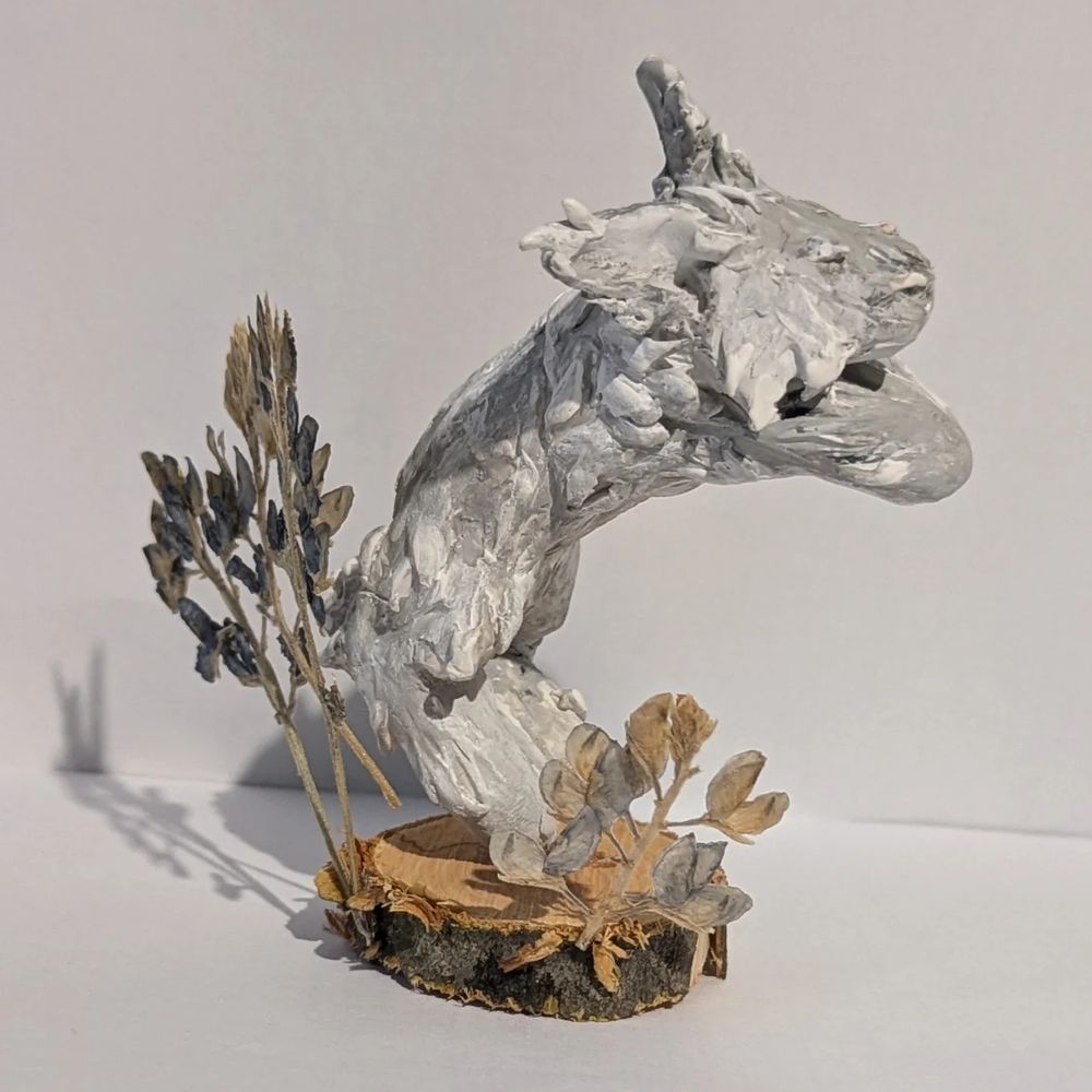 Clay Lionhead Rabbit figure. He's gray and "leaping" off of a wooden base surrounded by flowers.