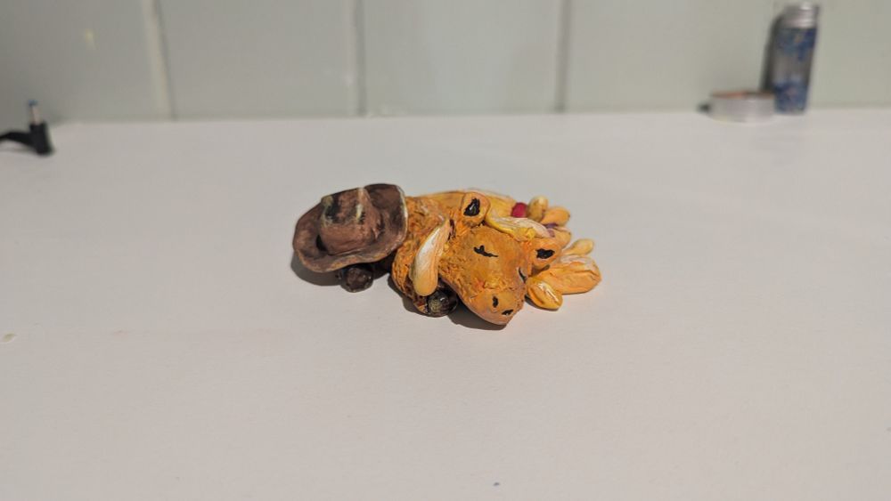 Front view of a stylized Applejack clay figure from the show MLP (My Little Pony) she's laying halfway on her side with her hat on her hind leg