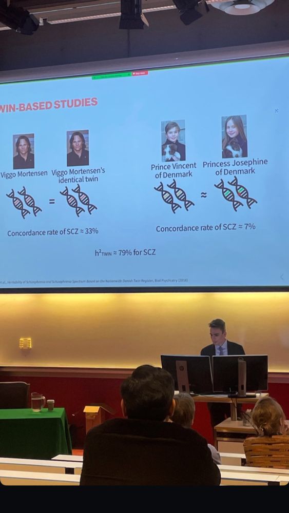 Photo of myself presenting at the trial lecture with a slide on twin-based studies in the background