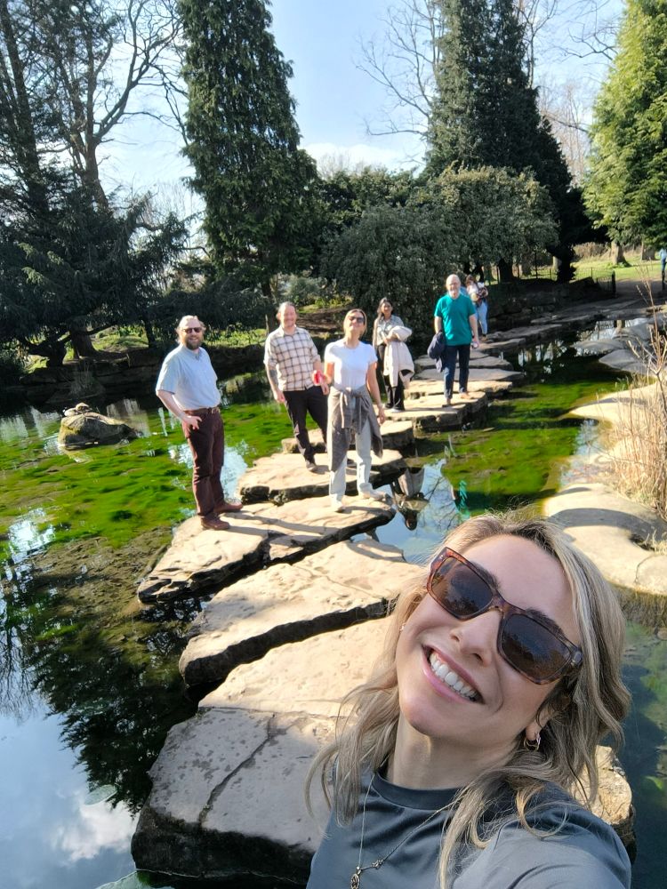 Six people standing happily smiling on stepping stones that cross Highfield park lake, Nottingham.