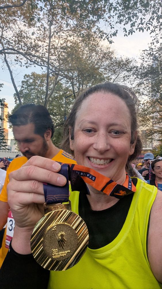 A selfie of me holding the nyc marathon finisher medal around my neck, exhausted and smiling