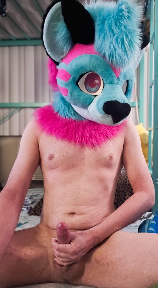Sitting on the ground in their fursuit head. The head is a blue, pink and black furred possum. They are completely naked otherwise. Their hand is on their dick that is very hard and looks like it is ready to fill someone. 