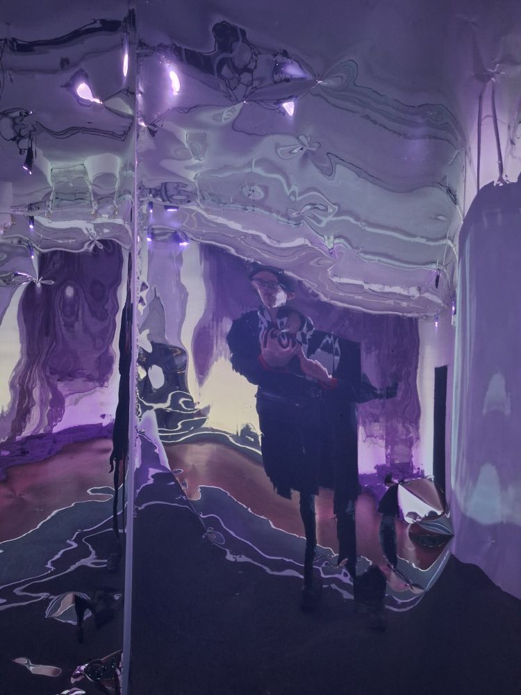 A distorted reflection of a woman wearing black one warped metal wall