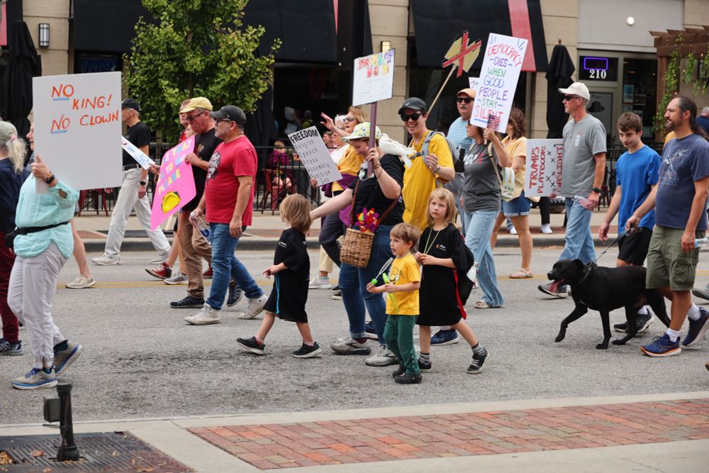 A family marches together in a crowd holding various protest signs. 