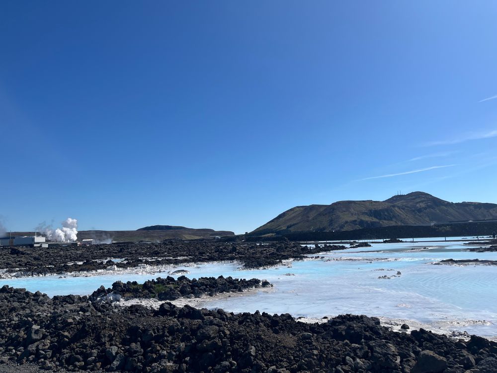 View of surreal landscape in Iceland.  Under a nearly cloudless blue sky, there are hills in the background that are a dark green.  At the far left is a geothermal plant with a puffy white cloud rising.  In the foreground is runoff from the plant:  warm, pale blue & whiteish pools of mineral-rich water.  The edges of the pool including the nearest point of the photo is dark black volcanic rock.

When I took this photo, I was filled with curiosity at such an unusual combination of colors & textures in the natural world + the human-made geothermal plant which does not introduce harm.  Instead, it contributes meaningfully.

All of this evokes calm and delight for me.