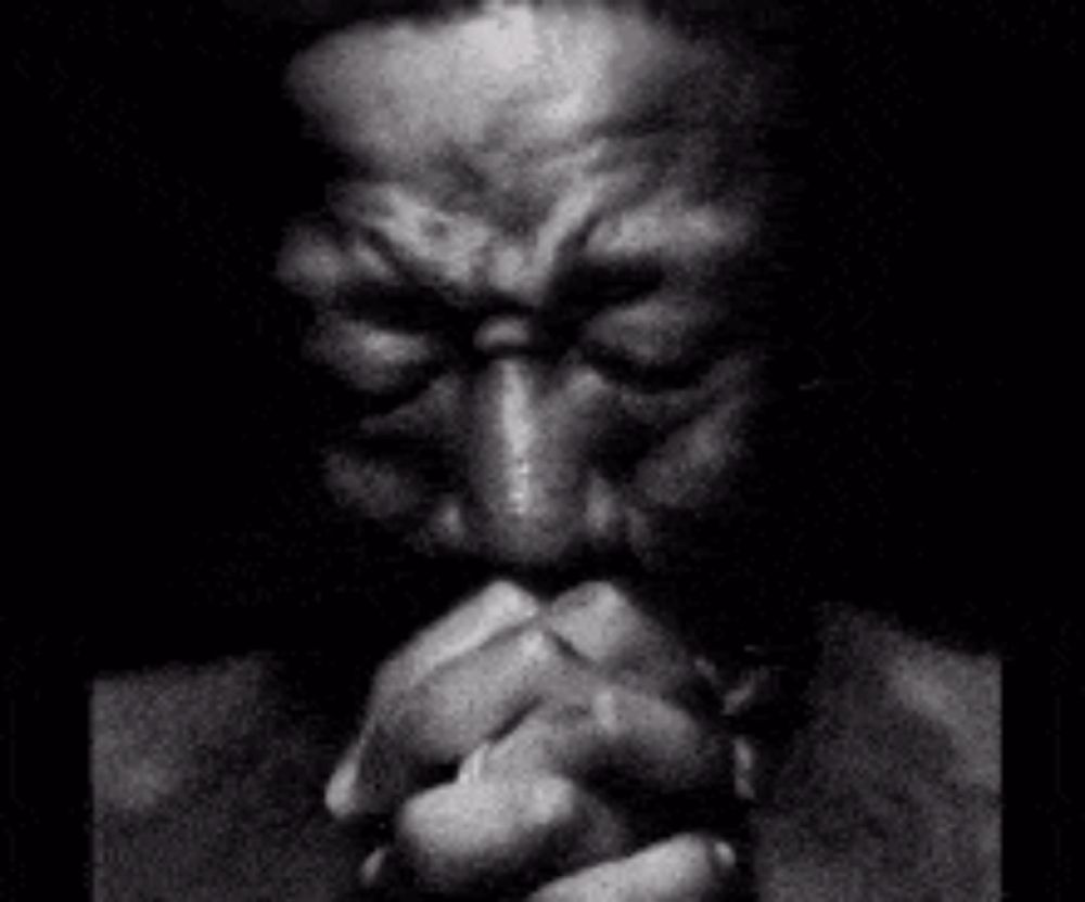 a black and white photo of a man praying with his hands folded in front of his face .