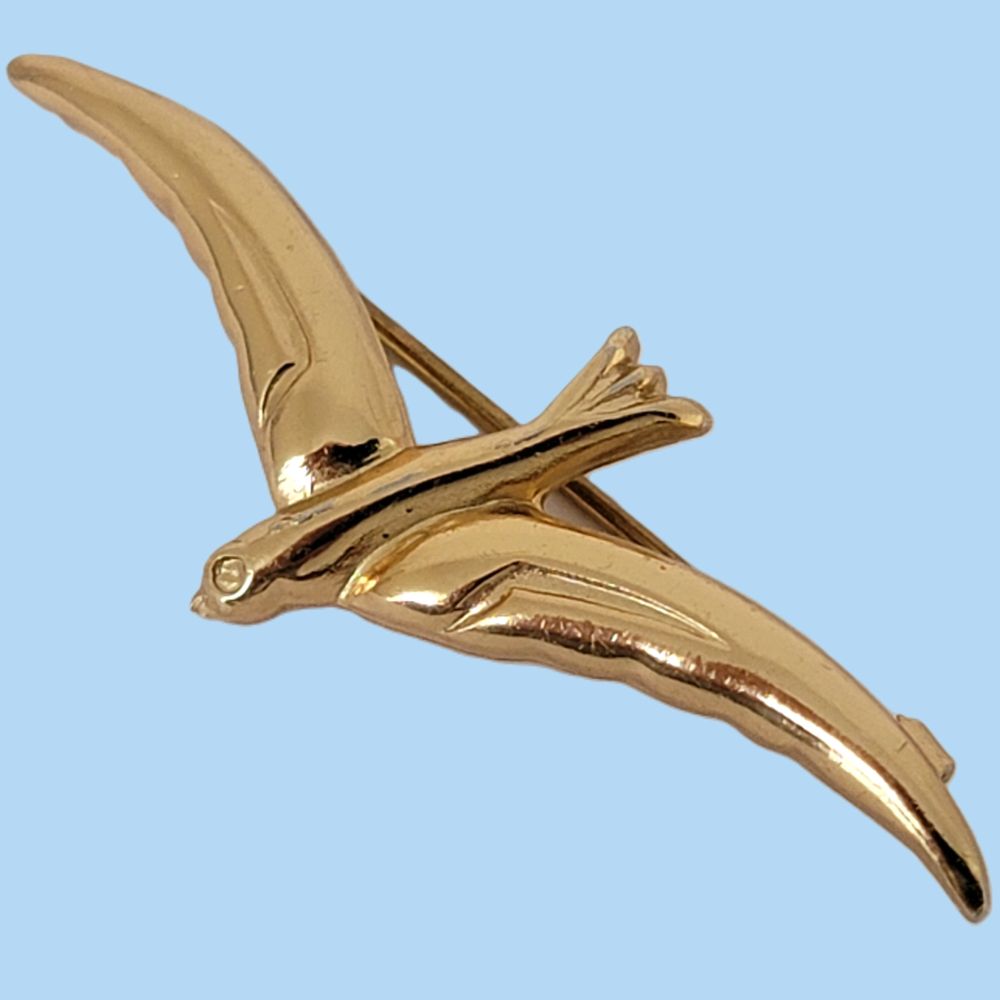 Gold tone tiny vintage bird pin on a blue background.