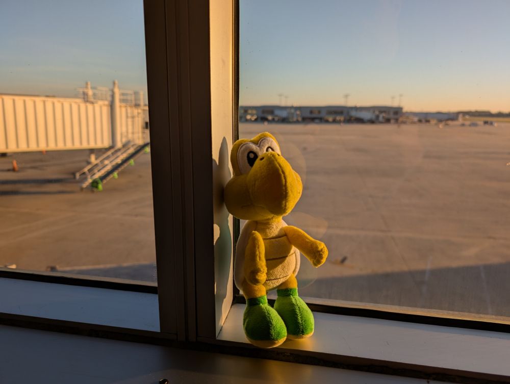 A green Koopa sitting on the window sill overlooking the airport gates.