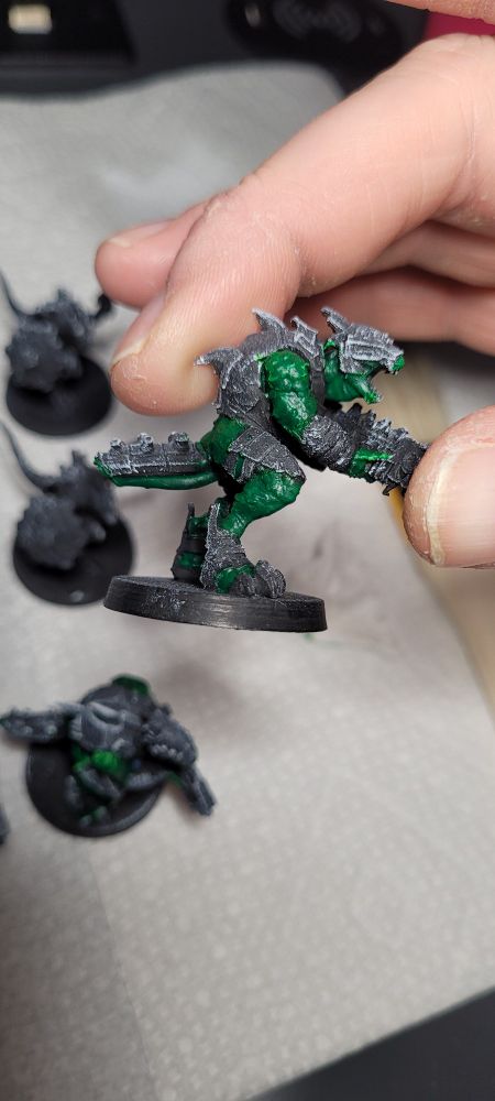 A 3D printed model of a lizard man holding a gun, being gripped by someone who needs more Aveno than humanity could possibly create. The model is only partially painted, and the lizard man has a noticeably better coverage of paint on its skin than the previous picture. Faintly in the lizard man's eye you can see hope for its future in fashion. However, it's tail is broken and the other lizard men tease him about it. Lizard Jessica left him over it, and he's had a hard month. He decided to put off dating for a while to focus on his book about lizard horticulture. It's not going well.