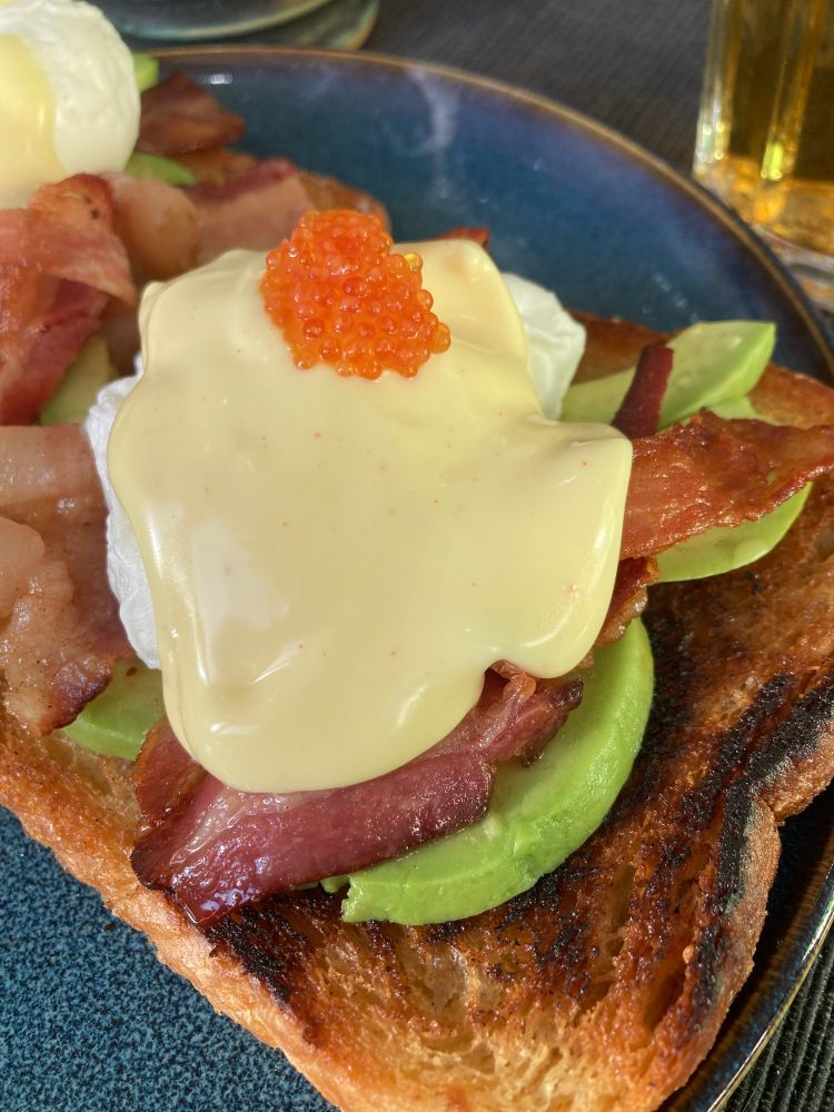En smörstekt macka med avokado, bacon, pocherat ägg, hollandaisesås och lite rom på toppen. 