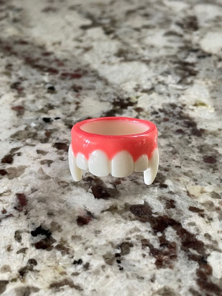photo of a plastic ring laying on a marble counter top. The ring is pink and white and resembles vampire teeth and gums.