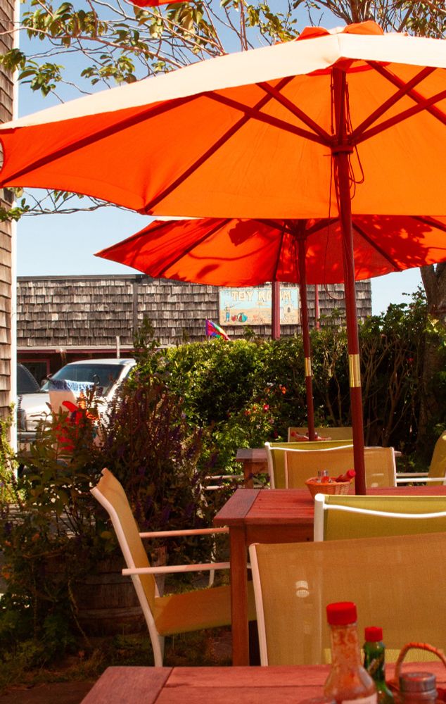 Photo of brunch tables outside of a diner in Oregon. The sunlight is hitting orange umbrellas over the tables, and it's creating this cool light effect where everything underneathe is really warm.