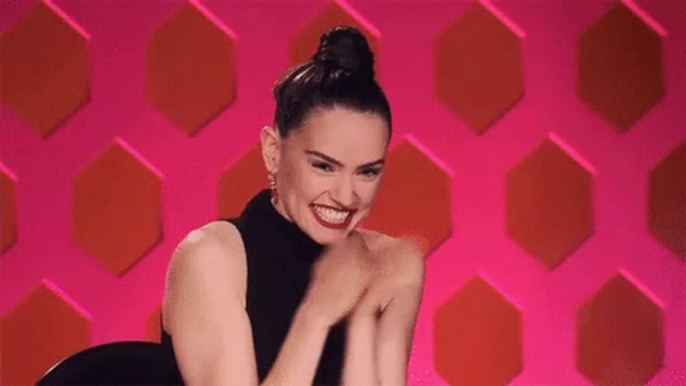 a woman in a black dress is smiling and clapping her hands in front of a pink background .