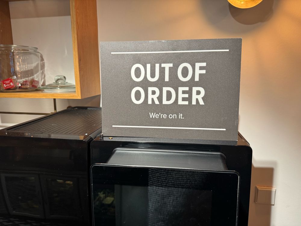 Defekte Kaffeemaschine mit Schild, auf dem „Out of order. We‘re on it.“ steht.