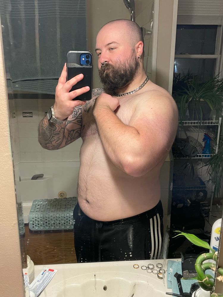 Same white transmasc, this time posing to flex a thicc arm