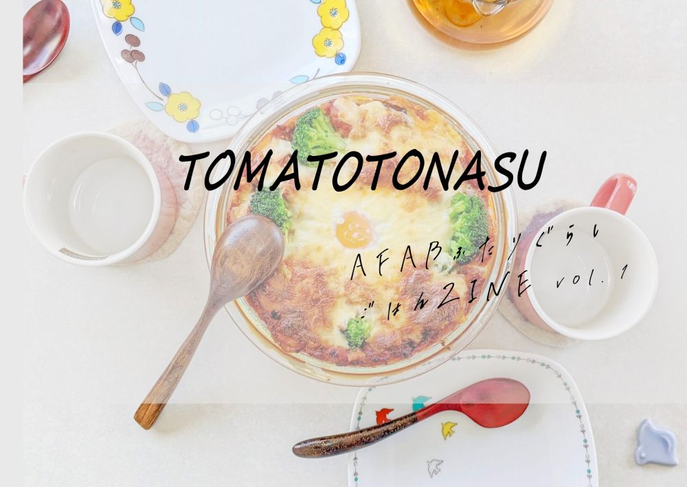 ZINEの表紙デザイン。テーブルに皿やカトラリーが並び、ブロッコリーと卵がのった焼き料理が中央に置かれている。中央上部に大きく『TOMATOTONASU』、その下に『AFABふたりぐらしごはんZINE vol.1』と手書き風の文字が添えられている。