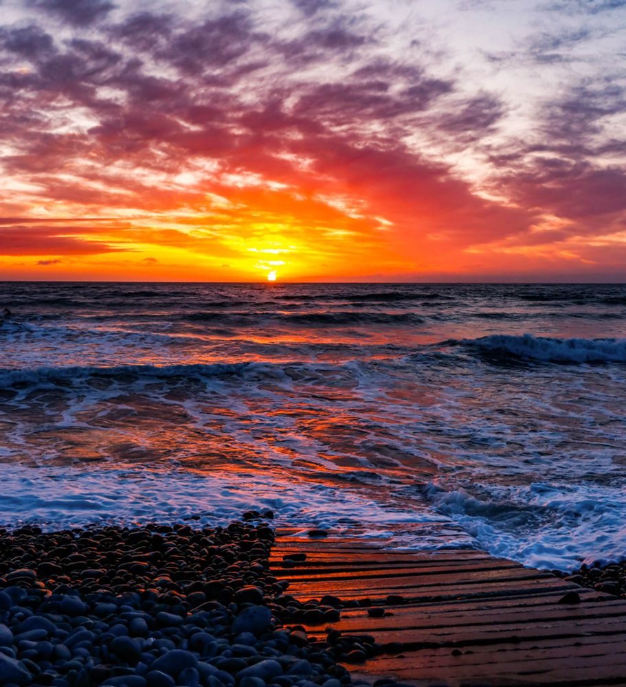 A beautiful orange sunset changing to red through the cloud spotted sky. Shining down on the high tide below. 