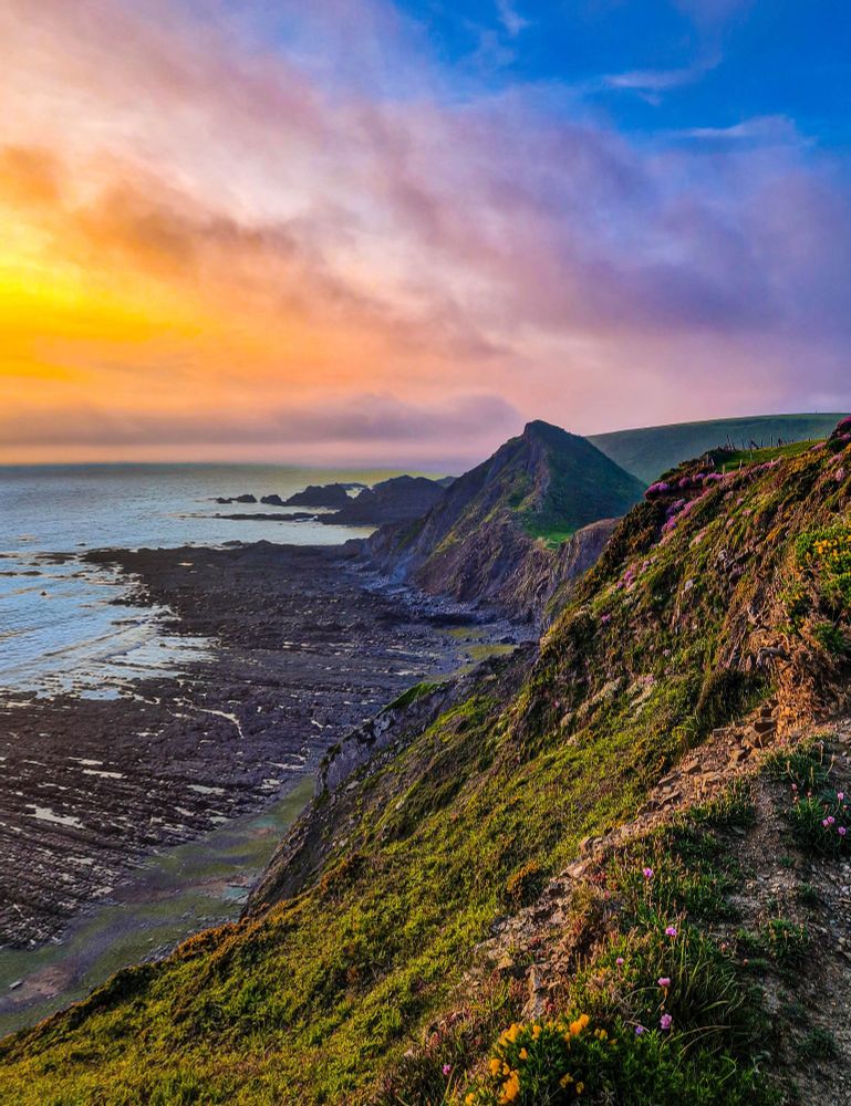 The rugged cliffs of the South West Coast Path under a misty sunset. 