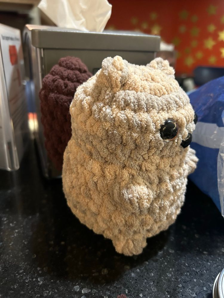 Photo of a beige and grey crocheted squirrel with a big brown tail facing to the side